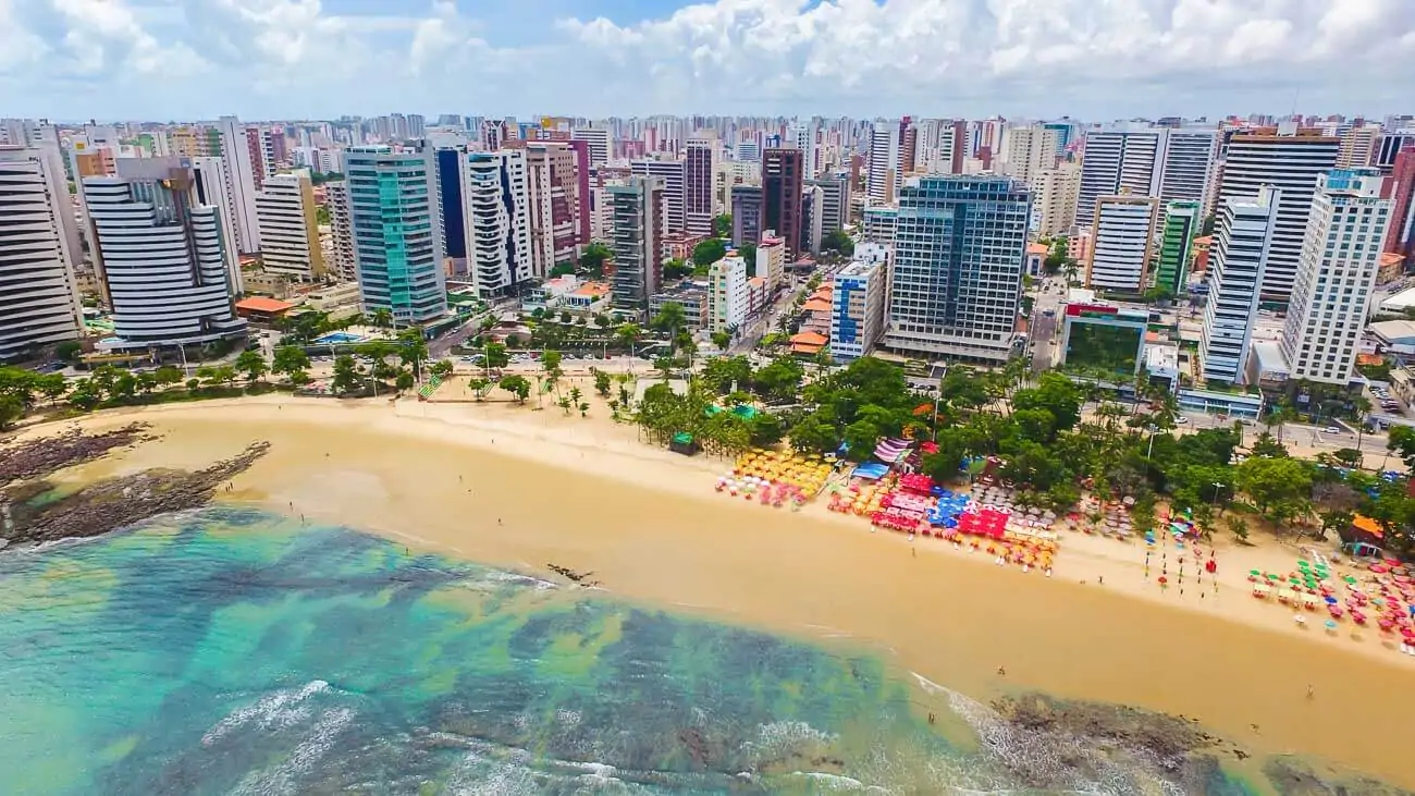 Vue aérienne de la plage de Meireles à Fortaleza, avec son sable fin, les vagues turquoise et les nombreux immeubles modernes de l'avenue Beira-Mar en arrière-plan.