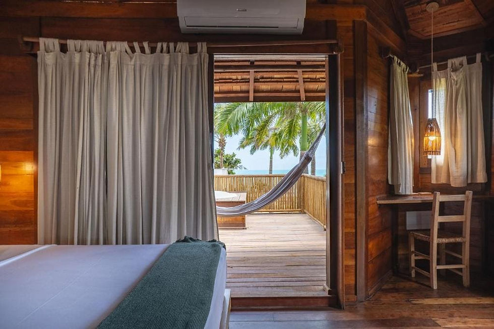 Intérieur en bois exotique d'une chambre de luxe à l'hôtel Hurricane à Jericoacoara, avec un lit au premier plan et une ouverture sur un balcon privé équipé d'un hamac, face aux palmiers et à l'océan.