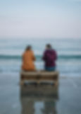 Two women sitting on a bench at the beach.