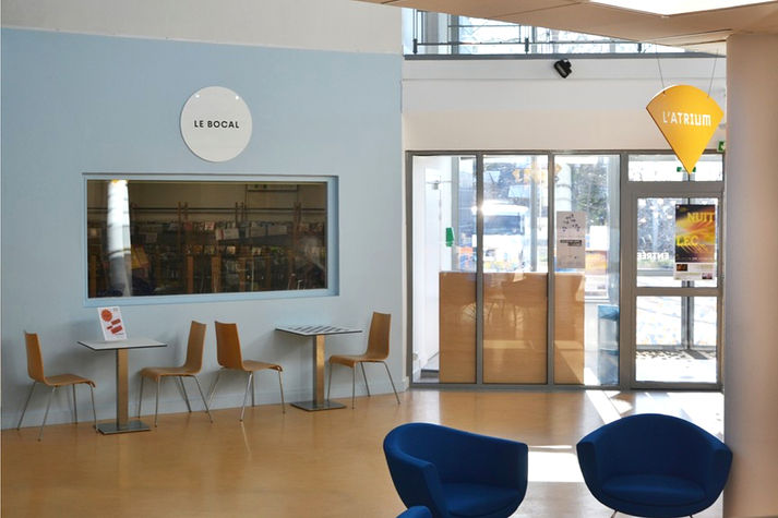 Une pièce avec des murs bleus et des éléments de signalétique (l'un blanc, l'autre orange). On trouve également des chaises et des tables, ce qui en fait un lieu d'échange et de rencontre.