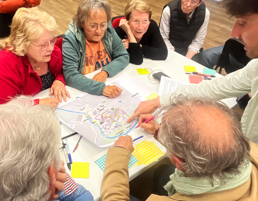 Groupe de participants identifiant et discutant des lieux et parcours sur une grande carte du centre-bourg.
