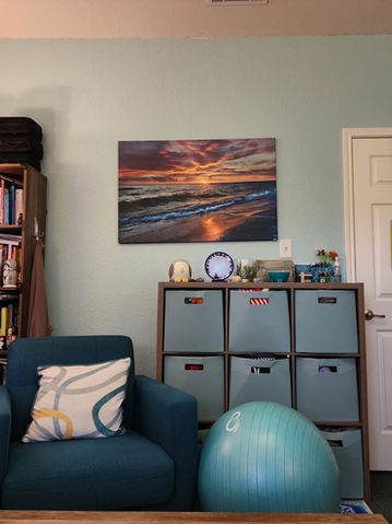 Serene therapy office: calming beach sunset art, books, and comfy chair