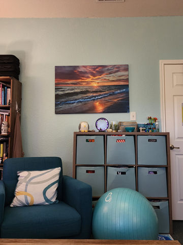 Serene therapy office: calming beach sunset art, books, and comfy chair