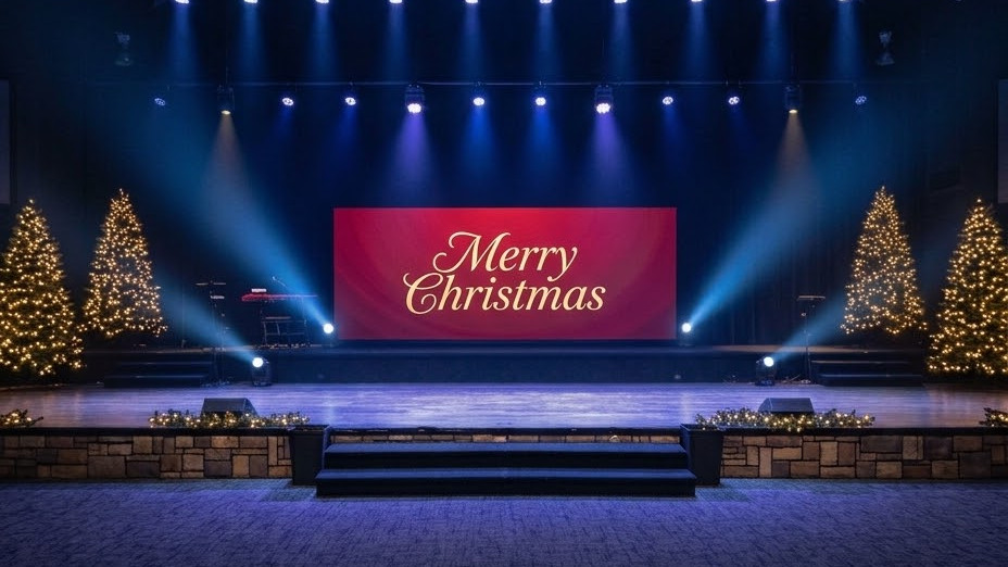 Christmas church stage with a simple manger and trees in front of an LED video wall showing a warm nativity sky.