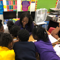 Teacher smiling, leaning over table with five young students in classroom.