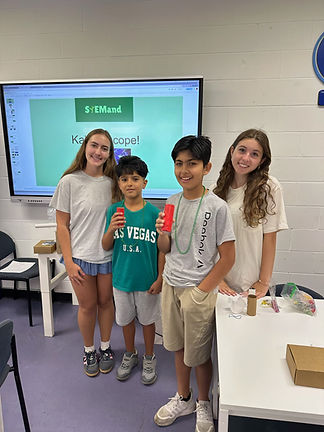 Two teen girl volunteers with 2 boys holding red kaleidoscopes