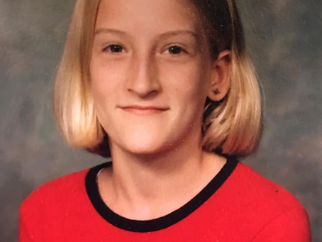 A kid smiling in front a grey background.