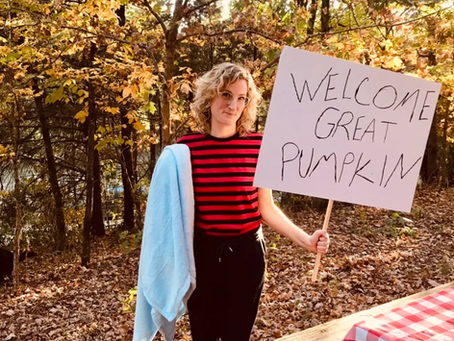 A woman holding a sign and a blanket with trees in the background.