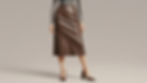 Person in a gray sweater and brown leather skirt, brown heels, standing against a plain beige background. Outfit is sleek and stylish.