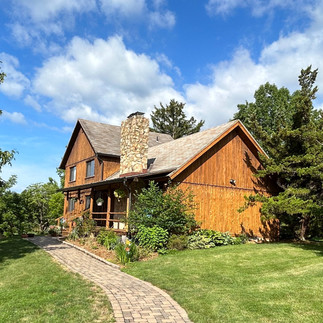 A summer view of the Meadowlark Ridge cabin with lush green trees and fluffy clouds in the blue sky.