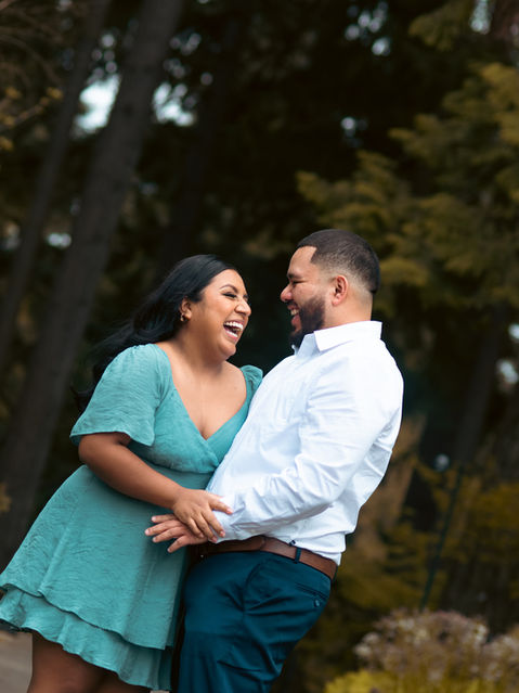 Laughing couple in embrace, enjoying each other, surrounded by nature and trees.