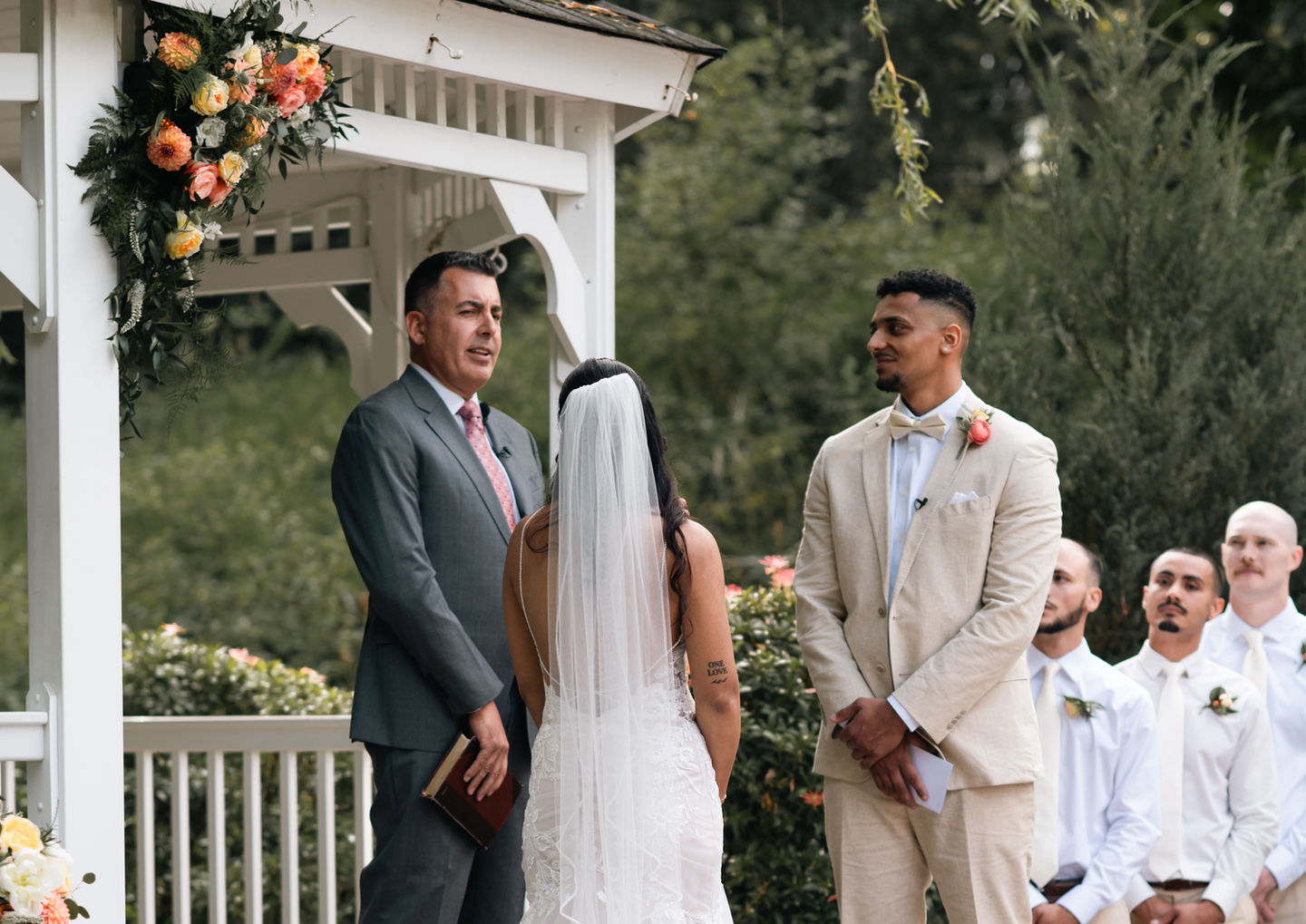 Bride and groom at altar. Wedding ceremony with groomsmen. White gazebo setting.