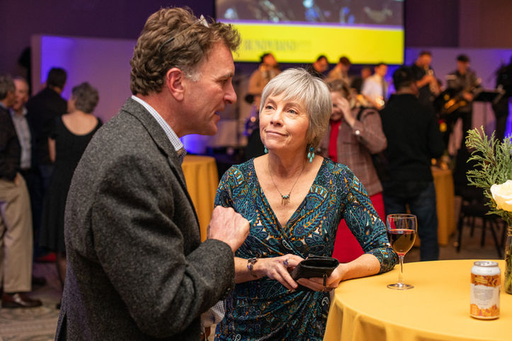 Two people talking at an event, many others in the background
