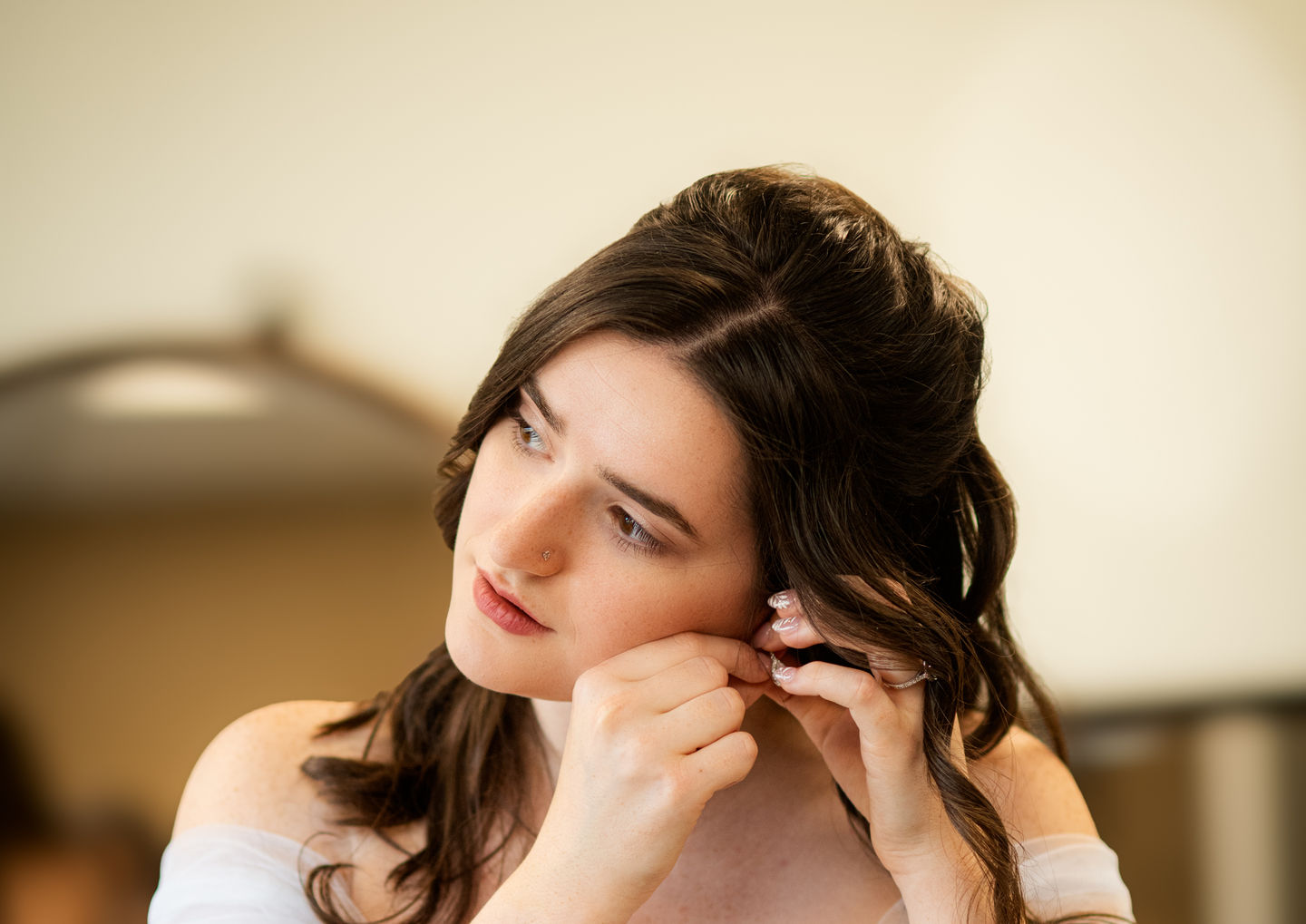 Bride adjusting her earring, wearing a white dress, getting ready for the wedding.