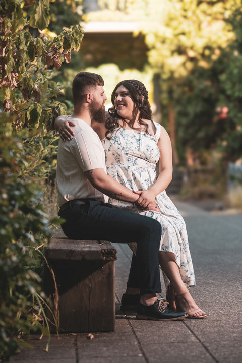 Couple sitting on a bench, smiling, holding hands, and enjoying a sunny day.