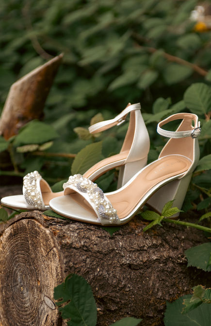 Elegant white bridal heels with embellishments showcased on a wooden log.