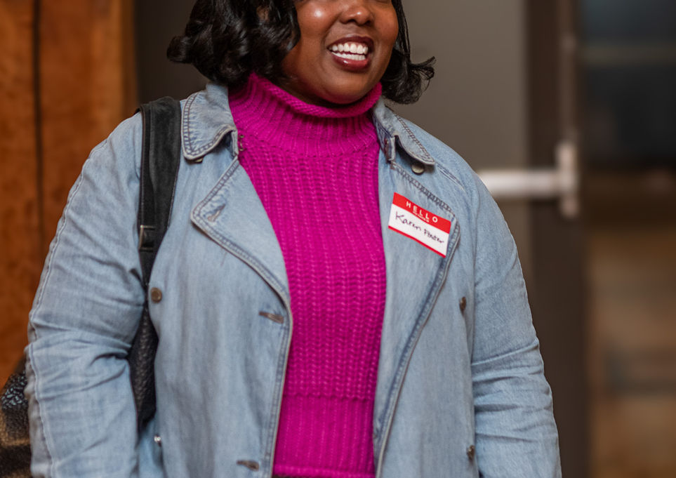 Smiling woman wearing pink sweater and blue coat smiles at a conference.
