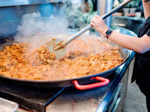 a large vessel of seafood paella being stirred by a chef from chowgirls catering