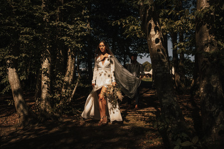 bride walking through a woodland holding her bouquet in the dappled sunlight holding her bouquet