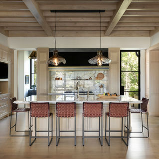A symmetrical frontal view of a luxury kitchen with a large marble-topped island, four woven barstools, and glass pendant lighting.