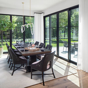 Modern European dining room with large black windows, contemporary lighting, luxury furnishings, and wooded outdoor views.
