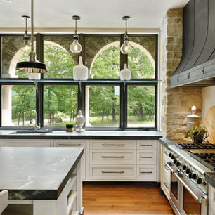 Luxury kitchen with oversized black-framed windows, stone walls, and modern transitional design.