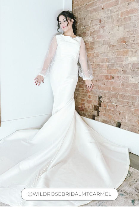 Bride wearing an Eddy K mermaid satin wedding gown that has ivory tulle bishop sleeves with pearl beading.