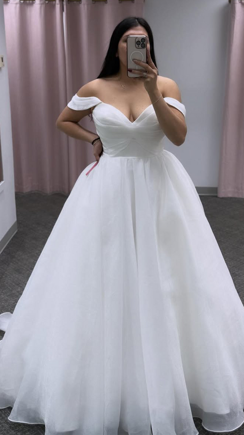 Brunette bride taking picture in the mirror while wearing a ballgown in ivory textured organza, off-shoulder swag sleeves, buttons to end of train. 

