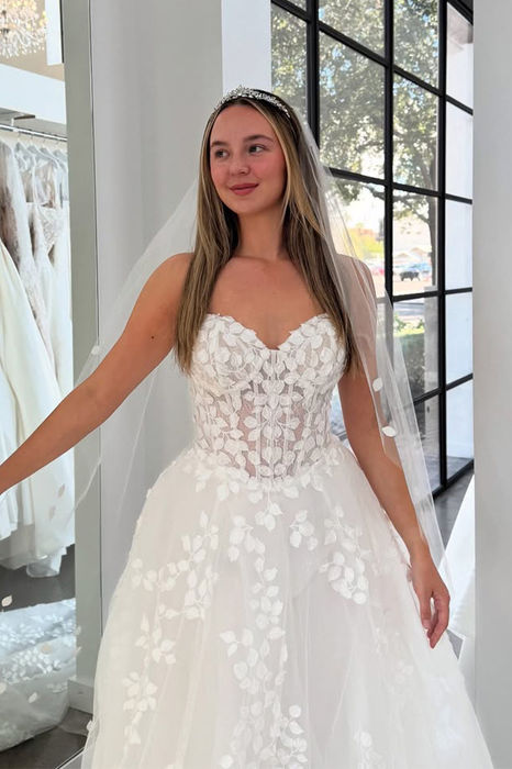 Bride with hand on her waist wearing an new eddy k wedding dress with 3D floral appliques.