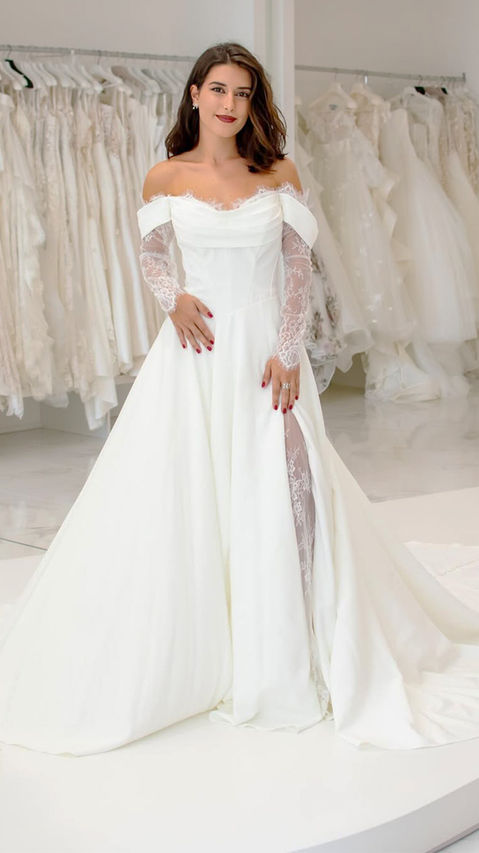 Brunette bride to be trying on an off-the-shoulder wedding gown with lace sleeves.