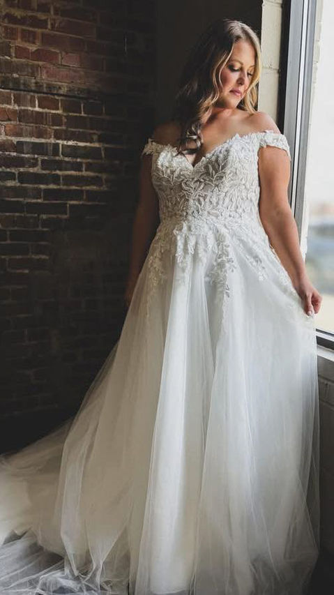 Bride standing next to window, wearing beautiful lace wedding gown.