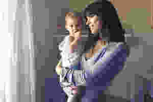 woman carrying baby boy wearing white tank top infront of white curtain inside the room