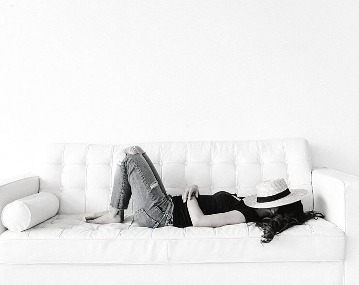 A woman lying down on a sofa with a sun hat covering her face