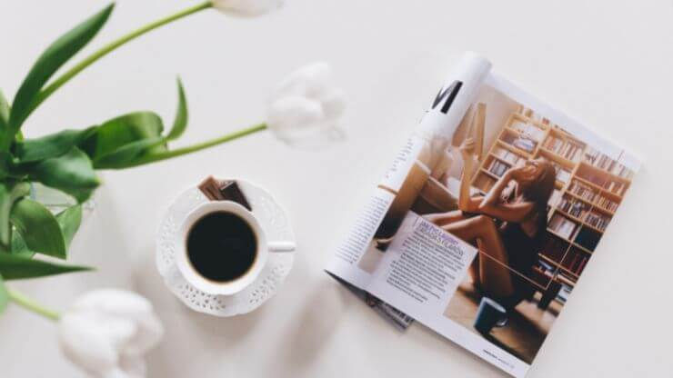 White flowers, a cup of coffee, and a magazine on a white table