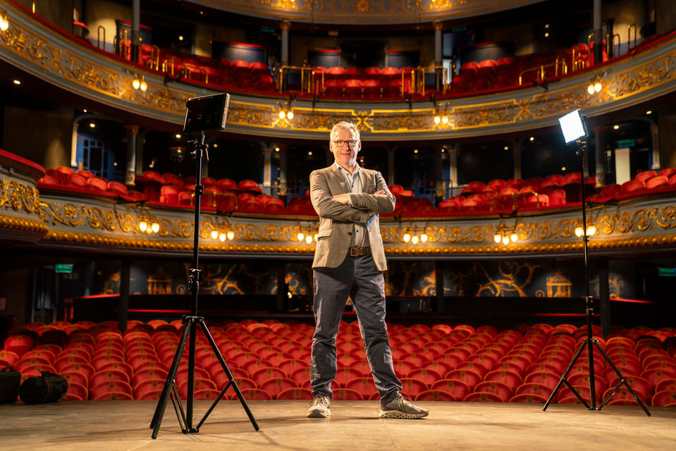 Portrait photograph of James Brining, theatre director, standing on the stage of Edinburgh's Royal Lyceum theatre with the theatre seats and balconies behind him