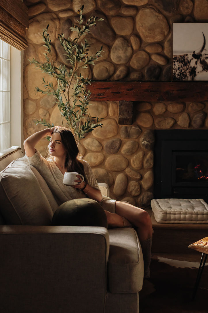Photo of model Rayne Ivanushka for The Orange Cabins LLC at The Bearstone Airbnb in Lake Arrowhead. The photo shows a model running her hands through her hair by the window on the couch. She's holding a coffee mug. Photo by Gianna Christina Photo. 