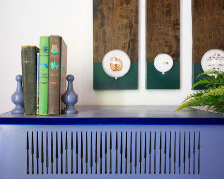 Custom doily-inspired radiator cover in muted purple, styled with vintage books, sculptural bookends, and nature-inspired wall art—an eclectic detail from a curated luxury interior.