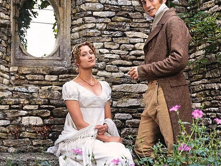 Charles Bingley standing near Jane Bennet, sitting, stone building in background