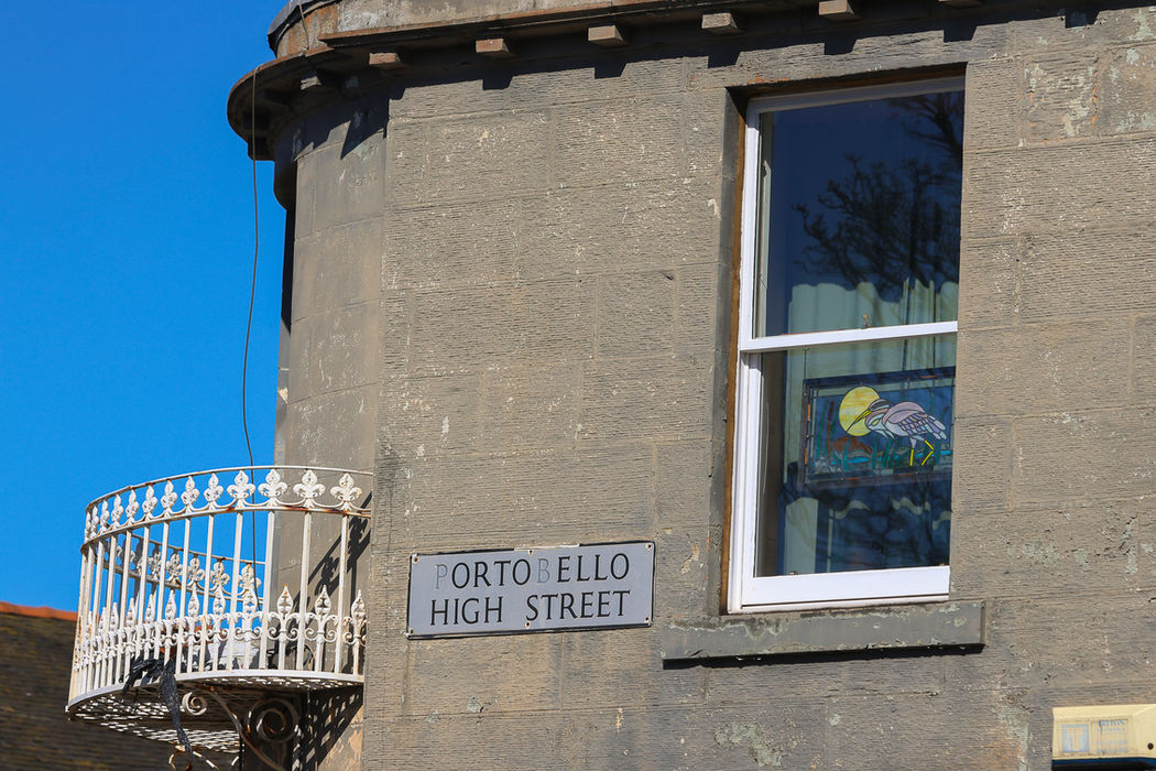 Orto Bello High Street sign on building exterior near a window.