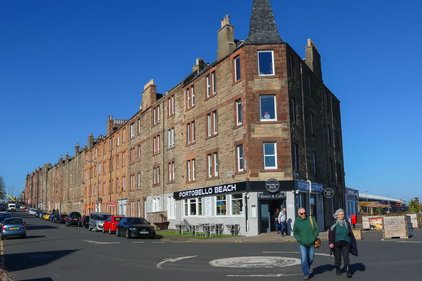 Apartment block with a shop and people on the street under sunny sky