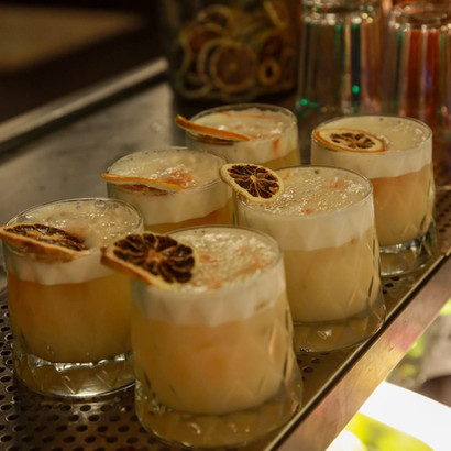 Several frothy cocktails with orange slices on a bar counter, ready.