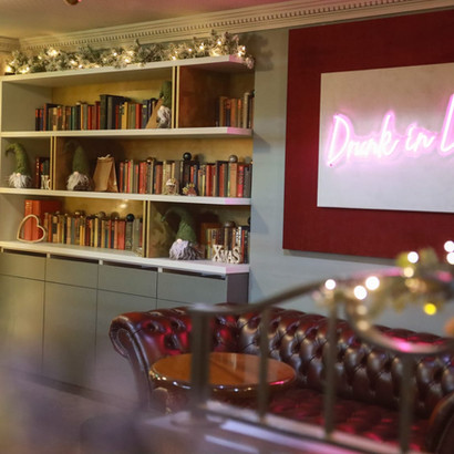 Cozy lounge with "Drunk in Love" neon sign, bookshelf, and chaise lounge.