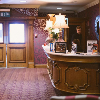 Hotel reception desk with lamps, "EXIT" sign, wooden doors, ornate decor.