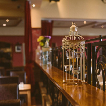 Elegant birdcage decoration on wooden bar inside a cozy restaurant setting.