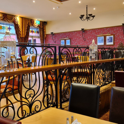 Interior of traditional restaurant bar with ornate railings, red wallpaper, comfortable seating.