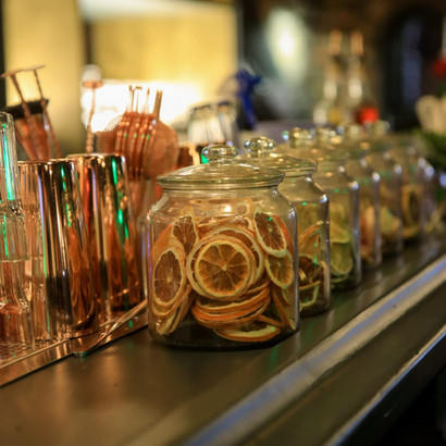Dimly lit bar counter with glasses, bottles, and dried orange slices.