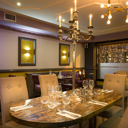 Elegant restaurant dining room with set table, chandeliers, and warm lighting.