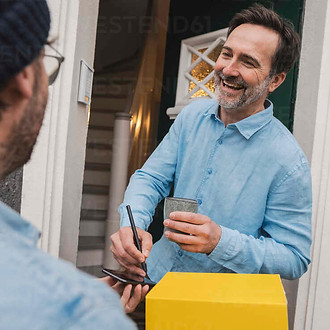 happy-customer-signing-and-receiving-package-from-delivery-person-at-doorway-JOSEF16809.jp