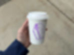 Hand holding a disposable coffee cup with a stamp on the side that reads "Wake The F Up - Broken Board Coffee"