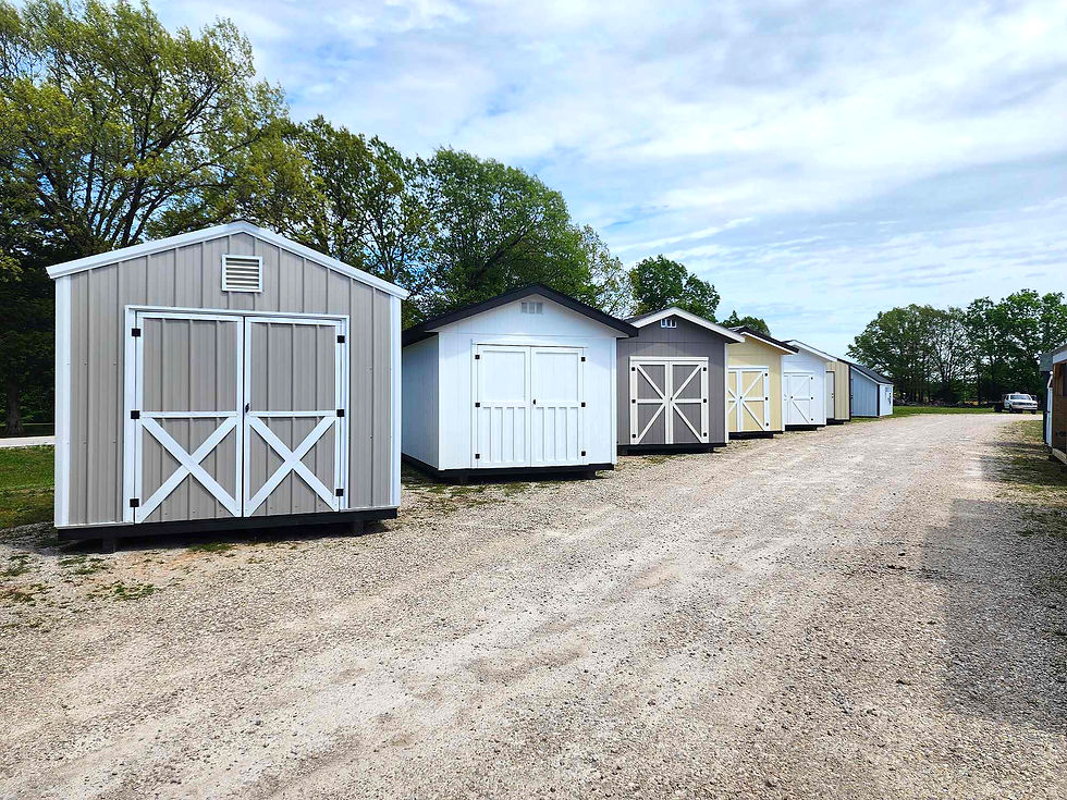Row of colorful storage sheds along a gravel drive under a bright cloudy sky, with green trees in the background